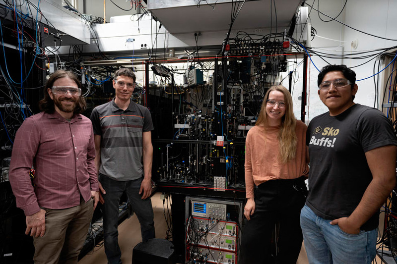(From left to right) Mason Marshall, David Hume, Willa Arthur-Dworschack and Daniel Rodriguez Castillo stand in front of the aluminum ion clock at NIST. With its recent improvements, the clock can pave the way for the campaign to redefine the second as well as explore new ideas in physics. Credit: R. Jacobson / NIST.