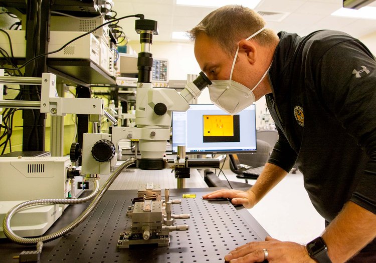 Steve Adamshick inspects an AIM/Spark Photonics EWD PIC chip.